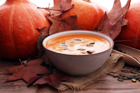 Roasted pumpkin and carrot soup with cream and pumpkin seeds on wooden background