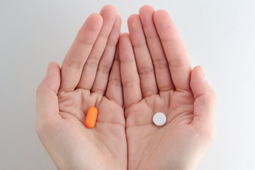 Man hands giving two big pills. White and orange. Make your selection. Health or ill. 