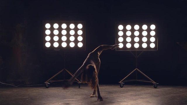 a young woman of pleasant appearance dances in the training hall in the lighting of searchlights in the background. the girl professional dance performs the set number in the style of classical and