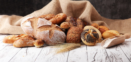 Assortment of baked bread and bread rolls on wooden table background.
