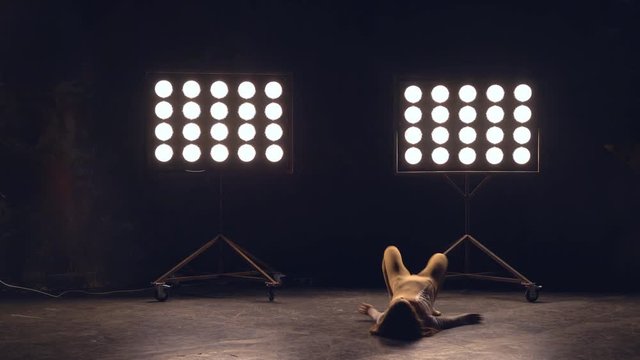 a young woman of pleasant appearance dances in the training hall in the lighting of searchlights in the background. the girl professional dance performs the set number in the style of classical and