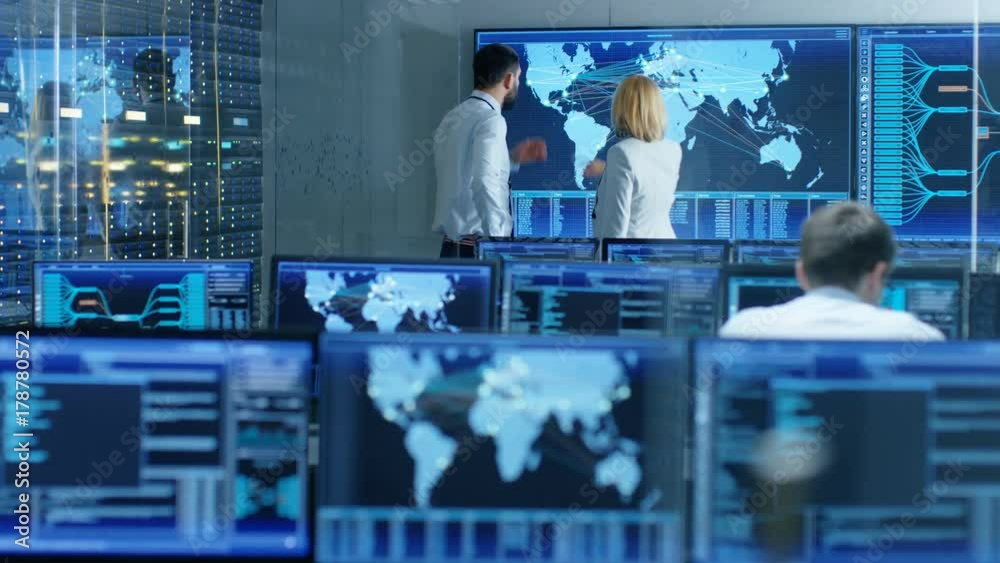 Poster In the System Monitoring Room Two Senior Operators Work on a Big Interactive Map. Facility is Full of Screens Showing Technical Data. Shot on RED EPIC-W 8K Helium Cinema Camera.