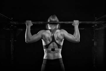 Young muscular woman doing pull up exercise in gym