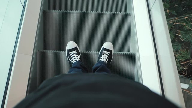 Closeup top view on man legs in sneakers traveler using moving escalator at airport terminal. Slow motion