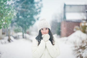 Fototapeta na wymiar Outdoor close up portrait of young beautiful happy smiling girl warming up her hands in snowfall. Christmas, New Year, winter holidays concept. Toned picture.