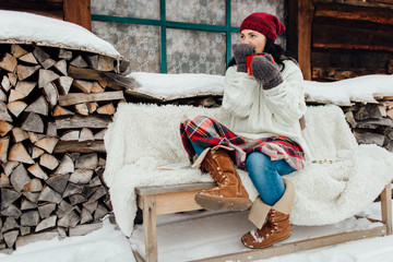 Woman sitting outside a cottage enjoying a snowy day on her own. Portrait of a woman feeling cold on a snowy winter day drinking a hot drink.