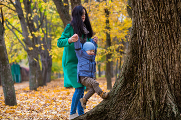 Mother with little son plays and smiles in park on background of colorful autumn fallen leaves