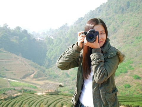Asian tourist woman backpacker taking photo at mountain nature view ,Chiang Mai , Thailand on holiday vacation. tea plantation at background