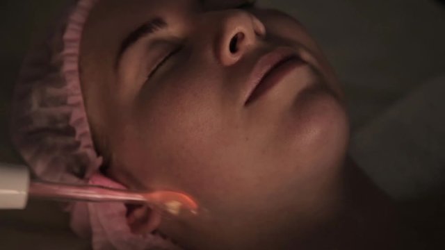 beautician does electric darsonval massage procedure for female client in a dark