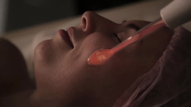 beautician does electric darsonval massage procedure for female client in a dark