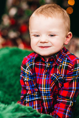 Stylish little boy sits on green armchair before a Christmas tree
