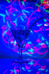 Glass with a straw cocktail with ice against a backdrop of abstract illumination of colored neon