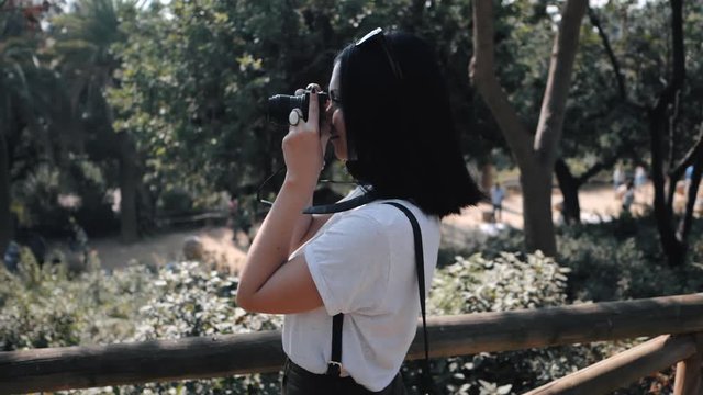 Beautiful young tourist brunette woman takes photos of nature in Barcelona park on small professional digital camera. Travel concept. Dolly shot, Slow motion