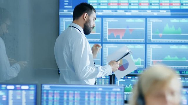 Walkthrough Stock Market Firm Traders Working with Clients, Papers, Trading Stocks and Bonds. Room is Full of People and Screens Showing Graphs and Ticker Numbers. 