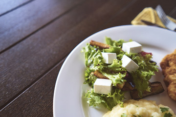 Tasty dinner. The chicken is battered. Salad. Puree. A white plate. Wooden table. A cafe
