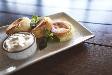 Curd cheese cakes. Greenery. Sour cream. A cafe. Dish. Wooden table. Breakfast