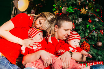 Fototapeta na wymiar Parents sit with twins in red suits before a Christmas tree