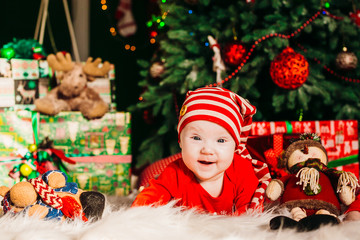 Fototapeta na wymiar Charming little child in red suit lies before a Christmas tree