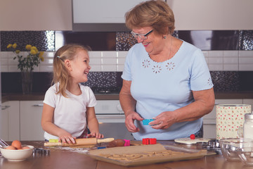 little girl and grandmother roll out the dough