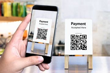 Qr code payment , online shopping , cashless technology concept. Coffee shop accepted digital pay without money , plastic tag on table and hand using mobile phone application to scan qr code.