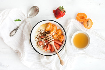 Fototapeta na wymiar Healthy breakfast set. Rice cereal or porridge with fresh strawberry, apricots, almond and honey over white rustic wood backdrop, top view