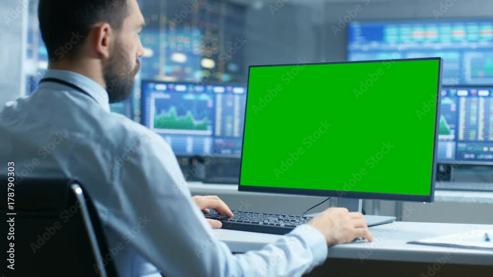 Aufkleber Over the Shoulder View of Stock Market Trader Working on a Computer with Isolated Mock-up Green Screen. In the Background Monitors Show Stock Ticker Numbers and Graphs.