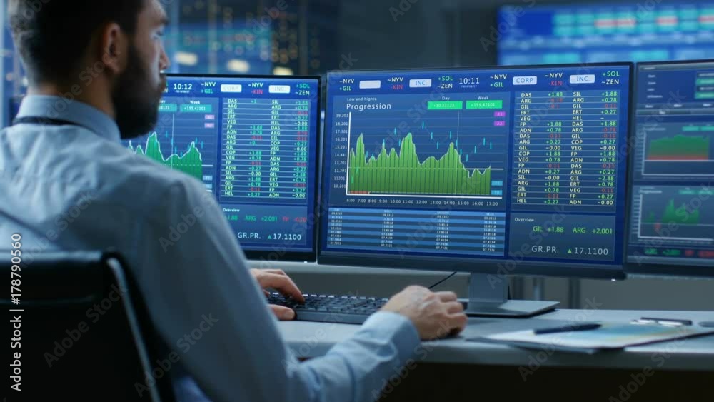 Poster Over the Shoulder View of Stock Market Trader Working on a Computer with Multiple Monitors Showing Stock Ticker Numbers and Graphs.  Shot on RED EPIC-W 8K Helium Cinema Camera.