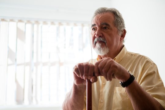 Thougtful Senior Man Looking Away While Holding Walking Cane