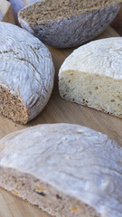 Vertical shot of different types of healthy, organic breads: brown, white, with nuts and seeds, cut in half, displayed on a wooden board, with selective focus