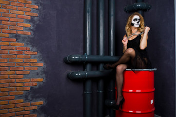Fototapeta na wymiar Halloween skull make up girl wear in black against sitting on red barrel at studio.