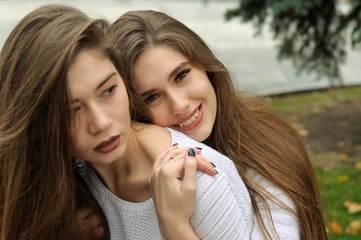 One girl hugs the other from behind, smiling