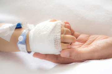 Closeup of hands of a little Boy attaching intravenous tube to patient's hand in hospital bed, And...
