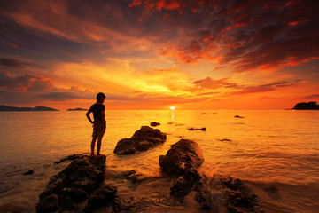 silhouette of young boy standing on rock in the sea with sunset sky, long speed exposure,Tarn-khu...