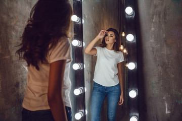 Sexy woman in a white t-shirt looks in the mirror. Mock-up.