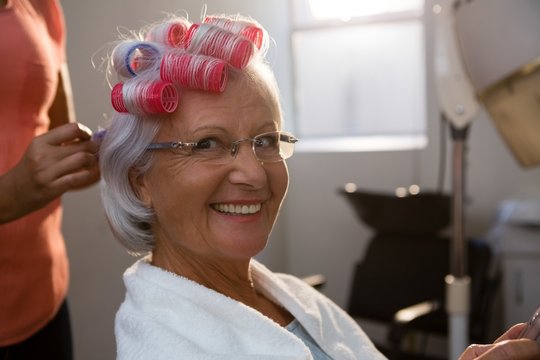 Cropped hands of hairstylist removing curlers from smiling woman