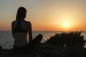 Fototapeta premium Sport girl meditating by the sea at sunset
