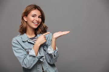Close-up portrait of young smiling brunette woman pointing with finger on her empty palm, looking...
