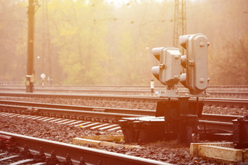 Photo of a fragment of a railway track with a small traffic light in rainy weather
