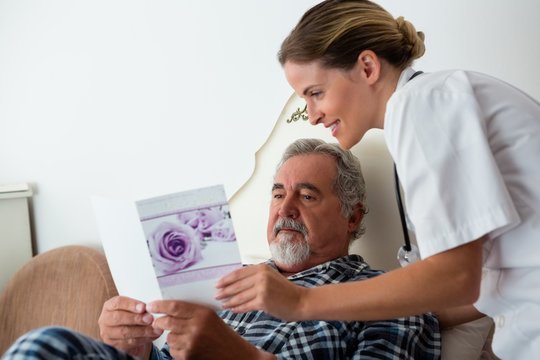 Female doctor showing get well card to patient relaxing on bed