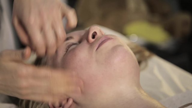 beautician does facial massage for beautiful woman in spa saloon.