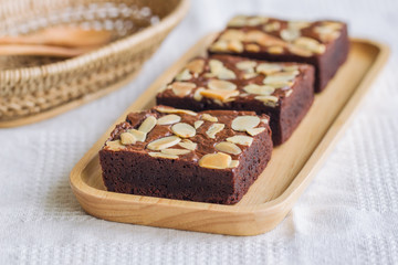 Homemade dark chocolate brownies topping with almonds slices and on wood plate put on white napkin. Delicious bitter,sweet and fudge. Brownie is one type of chocolate cake. Selective focus.