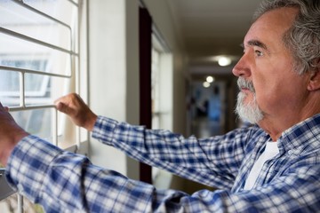 Fototapeta premium Thoughtful senior man looking through window at retirement home