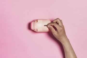 hand hold coin into coin bank on the pink background.