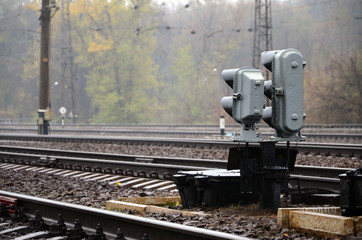 Photo of a fragment of a railway track with a small traffic light in rainy weather