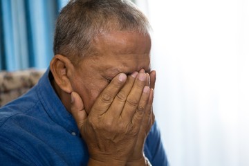 Close up of upset senior man covering eyes with hands