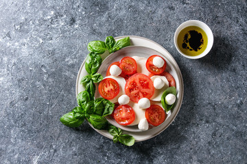 Italian caprese salad with sliced tomatoes, mozzarella cheese, basil, olive oil. Served in ceramic plate over gray texture background. Top view with copy space. Restaurant menu