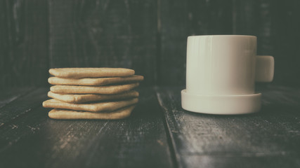 Background image of a small white cup of coffee and classic salty cracker on a brown wooden table with copyspace