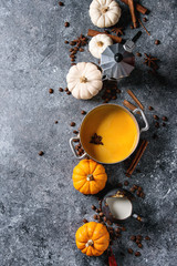 Ingredients for cook spicy pumpkin latte. Coffeepot, pumpkin milk in pan, jug of cream with spices, coffee beans and decorative pumpkins above over gray texture background. Top view, space.