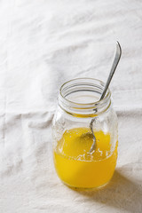 Glass of hot drawn ghee butter standing with spoon over white linen textile tablecloth. Healthy eating