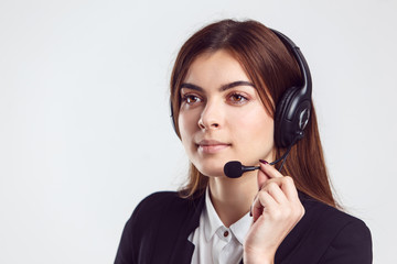 Cheerful brunette woman, kindly callcenter operator, wear black jacket and headphone set, smiling before white isolated background